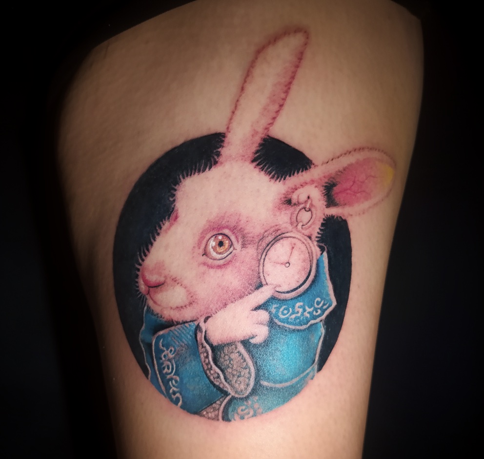 Tatuagem feminina realista do Coelho Branco de Alice no País das Maravilhas, estilo colorido e detalhado na perna, feita pelo tatuador feminino Cris Santos em Mogi das Cruzes e região. Realismo de animais e personagens.