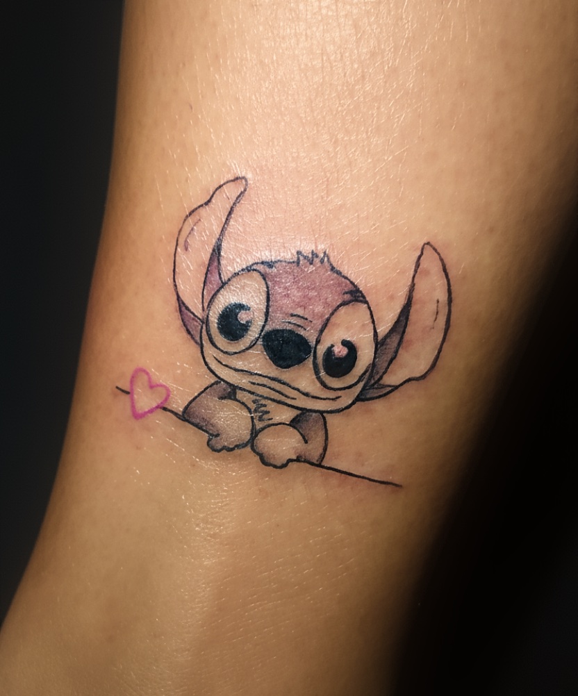 Tatuagem feminina delicada de coração de Stitch no braço, estilo colorido e delicado. Tattoo feminina no braço feita pelo tatuador feminino Cris Santos em Mogi das Cruzes e região.