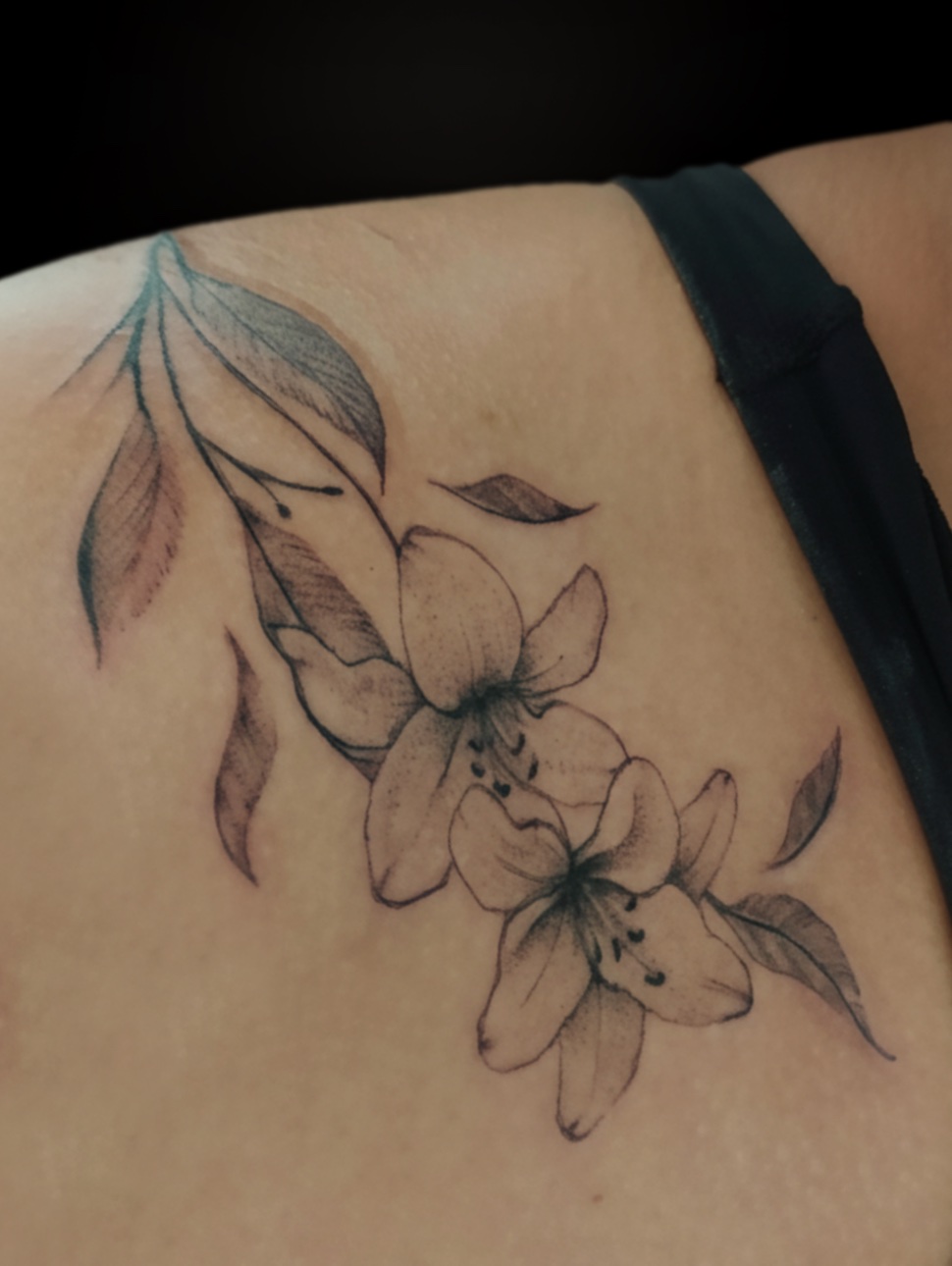 Tatuagem feminina de lírios em preto e cinza em realismo no ombro, feita pelo tatuador feminino Cris Santos em Mogi das Cruzes e região.